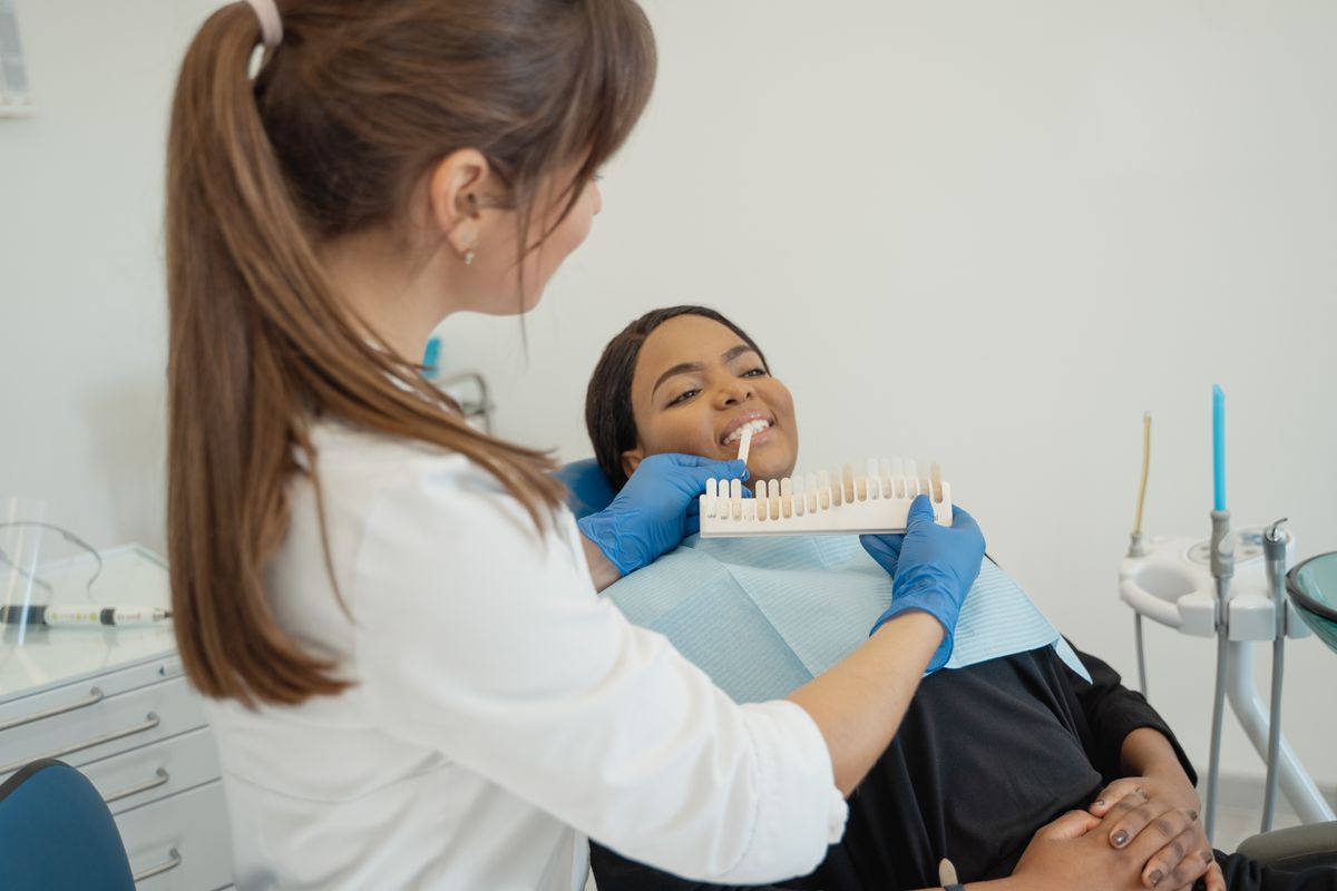 Una dentista compara una guía de tonos con la sonrisa de una paciente.